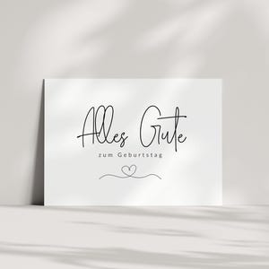May include: A white card with black text that reads "Alles Gute zum Geburtstag" with a small heart drawn below the text.