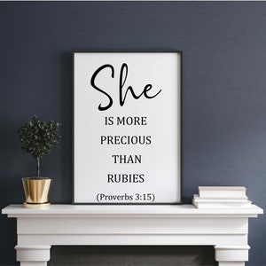 May include: A black and white print with the text "She is more precious than rubies (Proverbs 3:15)" on a white background. The print is framed and hanging on a wall.