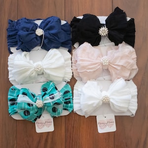 May include: Set of six fabric headbands with large bows and pearl embellishments. The headbands are in various colors including black, white, pink, blue, and teal with white polka dots.