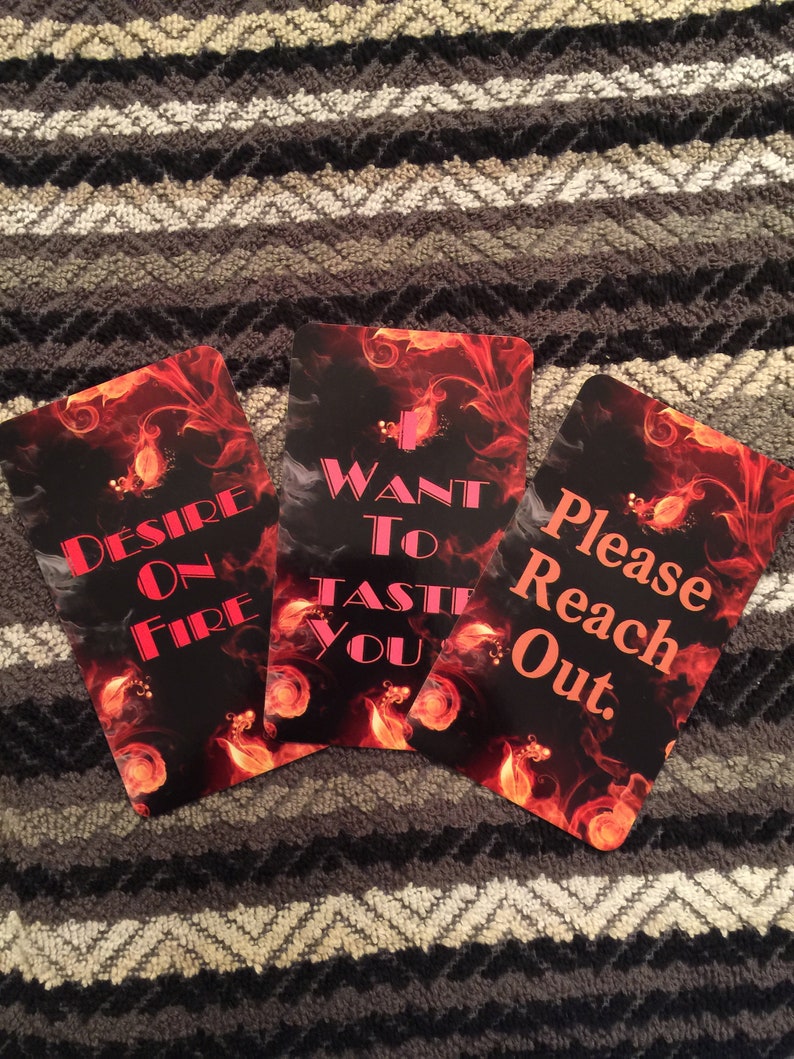 Puede incluir: Tres cartas con un fondo de fuego y texto rosa. La primera carta dice "Desire on Fire". La segunda carta dice "Want to Taste You". La tercera carta dice "Please Reach Out."