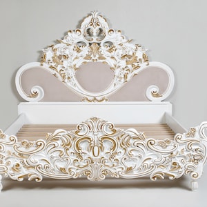 May include: White and gold ornate bed frame with a carved headboard and footboard. The headboard features a large, ornate design with a central panel that is upholstered in a light beige fabric.