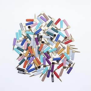 May include: A collection of colorful 3.5mm audio jack connectors. The connectors are in various colors, including red, blue, green, purple, and orange. The jacks have a gold-colored metal tip and a plastic sleeve. The image is taken on a white background.