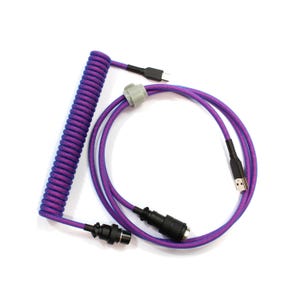 Può includere: Cavo USB viola e blu a spirale per tastiera meccanica. Il cavo ha un connettore USB-A, un connettore USB-C e un connettore staccabile. Il cavo è progettato per collegare una tastiera a un computer.
