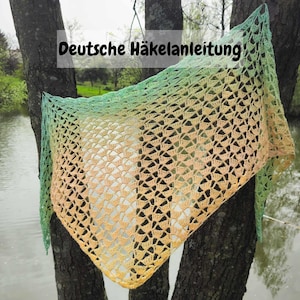 May include: A crocheted shawl with a gradient of green, yellow, and orange colors. The shawl is draped over a tree branch and the text "Deutsche Häkelanleitung" is visible at the top of the image.