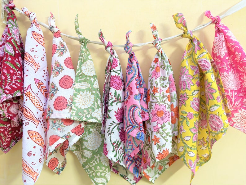 May include: A set of eight colorful cotton tea towels with floral and paisley patterns. The towels are hung on a string and are ready to be used.