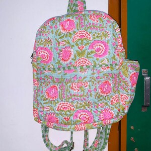 Puede incluir: Una mochila de color azul claro y rosa con estampado floral y correas verdes. La mochila tiene un dise&ntilde;o acolchado y una cremallera.