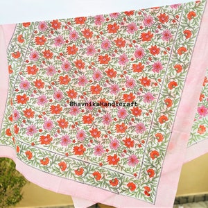 May include: A white cotton tablecloth with a pink border and a floral print featuring pink and orange flowers. The tablecloth is printed with the text "BhavnikaHandicraft".
