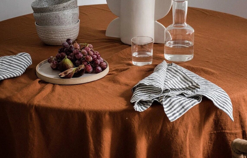 Może przedstawiać: Brązowy obrus lniany z białym ceramicznym talerzem z winogronami i figami, dwie prążkowane serwetki, przezroczysty szklany kieliszek z wodą i przezroczysta szklana butelka z wodą.