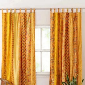 Op de afbeelding: Een paar gele en oranje gepatroneerde gordijnen met een geometrisch ontwerp. De gordijnen zijn gemaakt van een zachte, lichtgewicht stof en hebben een ontspannen, bohemian stijl.