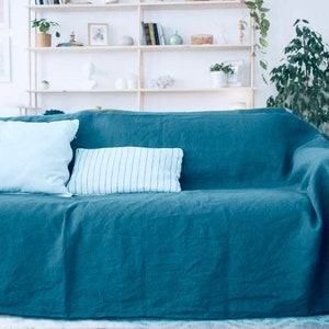 Puede incluir: Un sofá azul turquesa con dos almohadas azul claro y una almohada a rayas blancas y azules. El sofá está cubierto con una manta de tiro azul turquesa.