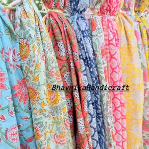 May include: A collection of colorful cotton fabric scarves with floral patterns. The scarves are hanging on a clothesline and have a variety of colors, including blue, green, pink, yellow, and orange. The text "Bhavnaka Handicraft" is visible on the scarves.