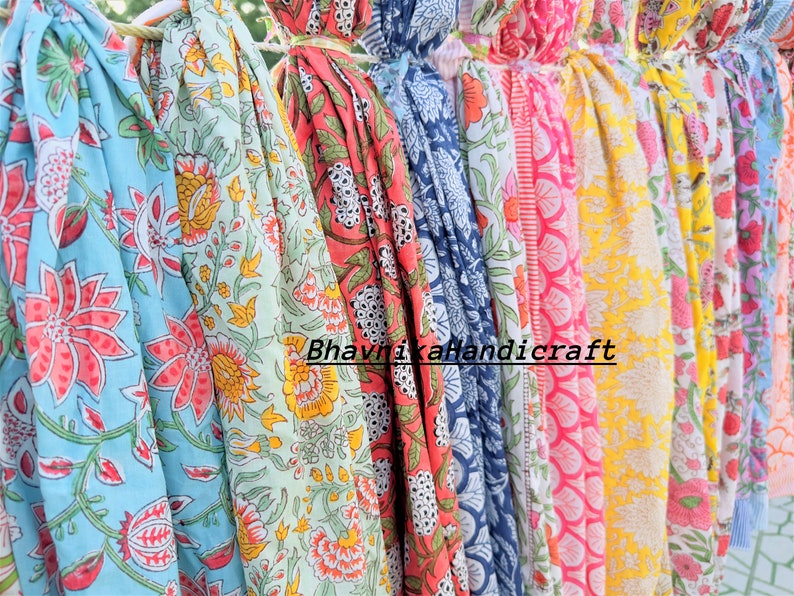 May include: A collection of colorful cotton fabric scarves with floral patterns. The scarves are hanging on a clothesline and have a variety of colors, including blue, green, pink, yellow, and orange. The text "Bhavnaka Handicraft" is visible on the scarves.