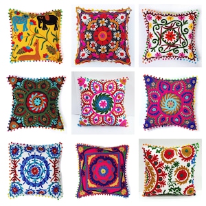 May include: Nine colorful embroidered throw pillow covers with pom-pom trim. The pillows feature a variety of floral and geometric designs in shades of red, blue, green, yellow, and pink.