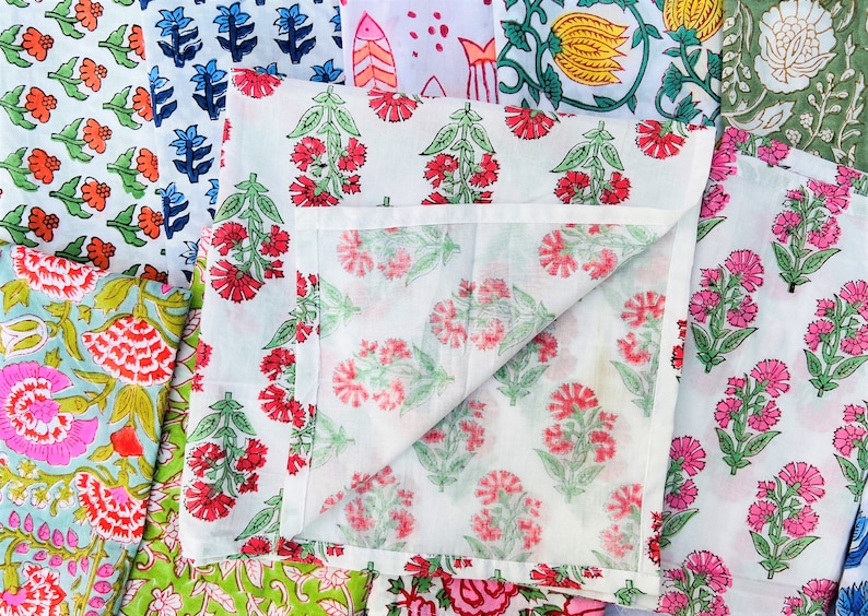May include: A collection of fabric squares with floral patterns in various colors, including pink, red, blue, green, and yellow. The fabric squares are folded and arranged in a pile.