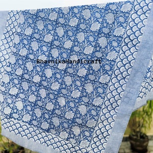May include: A blue and white cotton fabric with a floral pattern. The fabric has a border with a scalloped design. The text "BhavnjikaHandicraft" is printed on the fabric.