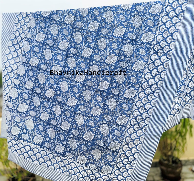 May include: A blue and white cotton fabric with a floral pattern. The fabric has a border with a scalloped design. The text "BhavnjikaHandicraft" is printed on the fabric.