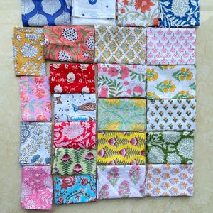 May include: A collection of folded fabric squares with various floral and geometric patterns. The color palette includes blues, pinks, yellows, greens, and reds. The fabrics are arranged in a grid, showcasing the diverse designs.