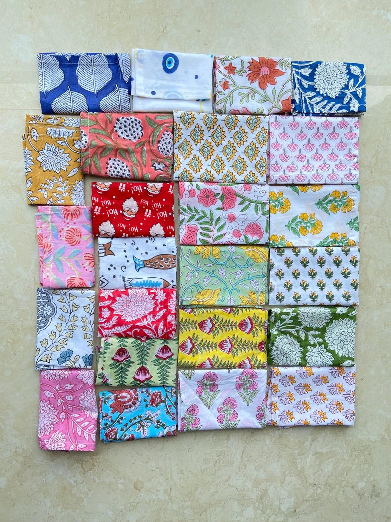 May include: A collection of folded fabric squares with various floral and geometric patterns. The color palette includes blues, pinks, yellows, greens, and reds. The fabrics are arranged in a grid, showcasing the diverse designs.