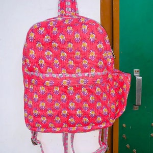Puede incluir: Una mochila acolchada rosa con estampado floral y correas a rayas. La mochila tiene un peque&ntilde;o bolsillo lateral.