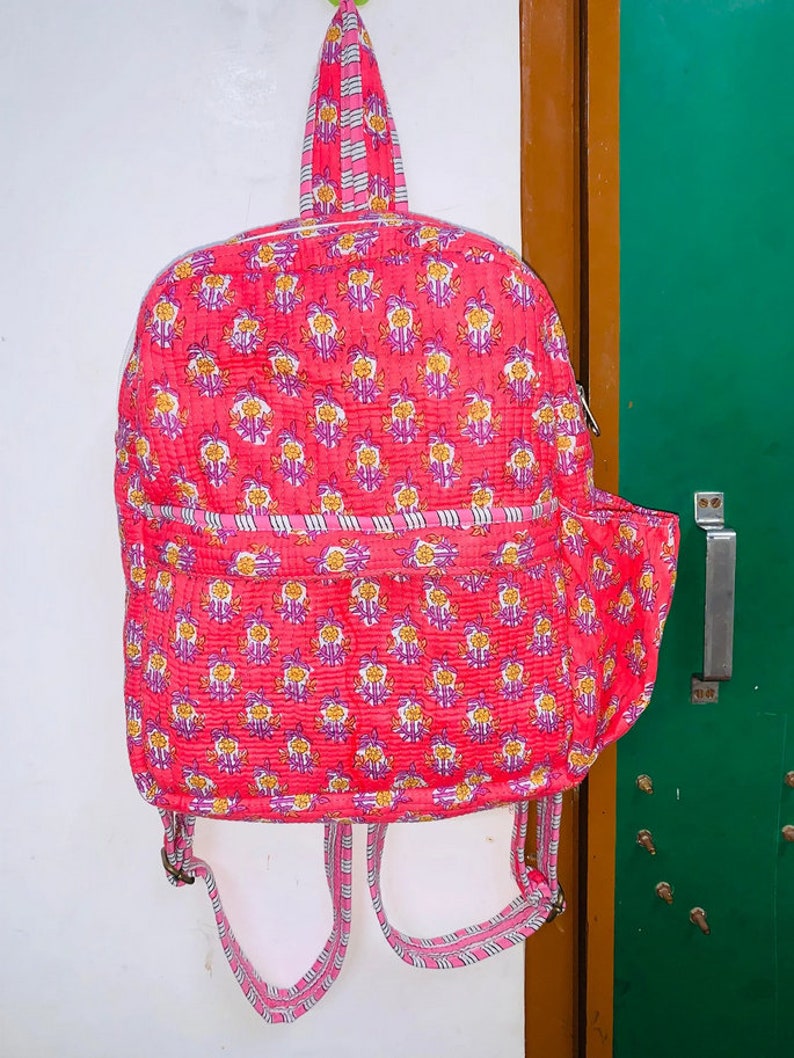 Puede incluir: Una mochila acolchada rosa con estampado floral y correas a rayas. La mochila tiene un peque&ntilde;o bolsillo lateral.