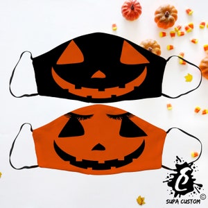 Peut inclure: Deux masques sur le thème d'Halloween. L'un est noir avec un visage de citrouille orange. L'autre est orange avec un visage de citrouille et des cils fermés. Les masques ont des boucles d'oreilles blanches. Des citrouilles décoratives et des bonbons sont éparpillés.