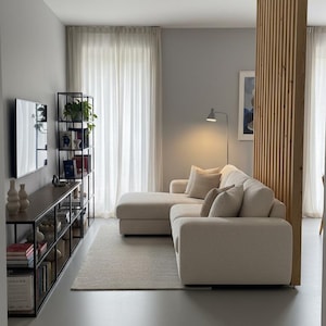 Peut inclure: Un salon comprenant un canap&eacute; d'angle couleur cr&egrave;me avec une m&eacute;ridienne, une &eacute;tag&egrave;re en m&eacute;tal noir avec des livres et de la d&eacute;coration, une console en bois fonc&eacute;, un tapis clair et un s&eacute;parateur de pi&egrave;ce &agrave; lattes de bois verticales.