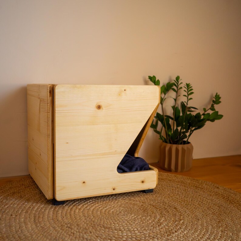 Pu&ograve; includere: Un letto per cani in legno con un bordo rialzato e un'apertura per un letto per animali domestici. Il letto &egrave; realizzato in legno naturale e ha un design semplice e moderno.
