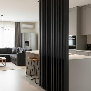 Peut inclure: Un s&eacute;parateur de pi&egrave;ce du sol au plafond compos&eacute; de lattes de bois verticales noires. La structure se situe entre un espace cuisine avec un &icirc;lot gris clair et un salon comprenant un canap&eacute; d'angle gris fonc&eacute; et une table basse claire.