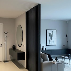 Peut inclure: Un s&eacute;parateur de pi&egrave;ce &agrave; lattes verticales noires se trouve entre un couloir et un salon. Le couloir comprend une console noire suspendue, un miroir rond et un porte-manteau. Le salon contient un canap&eacute; gris, un meuble TV noir et des tables.