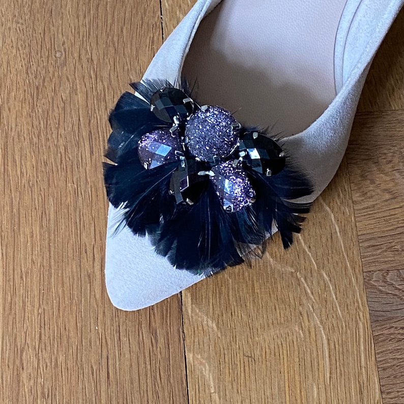 May include: A pair of beige ballet flats with a black feather and rhinestone embellishment.