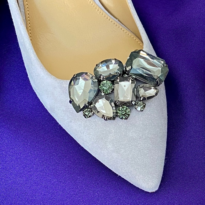 May include: A white shoe with a cluster of grey and green rhinestones on the toe.