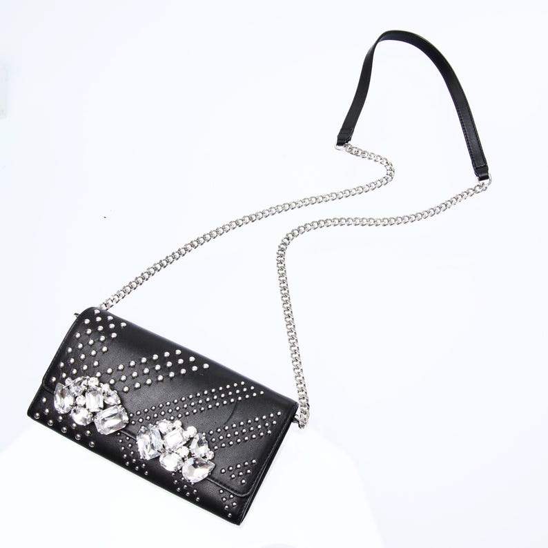 May include: A black leather clutch bag with a silver chain strap and a large rhinestone embellishment.