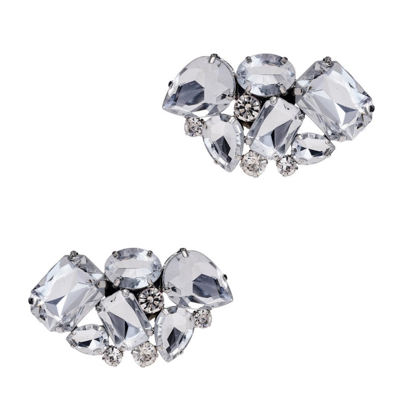 May include: Two pairs of clear crystal shoe clips in a heart shape. Each clip features a cluster of rhinestones and clear crystals.