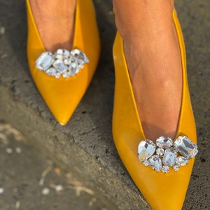 May include: A pair of yellow pointed-toe flats with a large rhinestone embellishment on the toe.