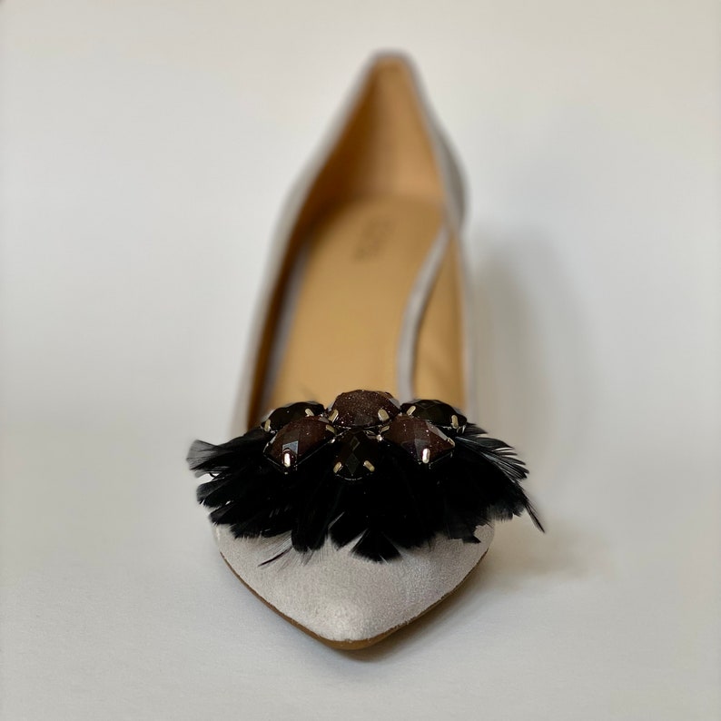 May include: A pair of grey suede pumps with a black feather and jewel embellishment on the toe.