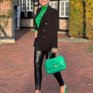 May include: A woman wearing a green turtleneck sweater, a black blazer, black leather trousers, and green heels. She is carrying a green quilted handbag with a gold chain strap.