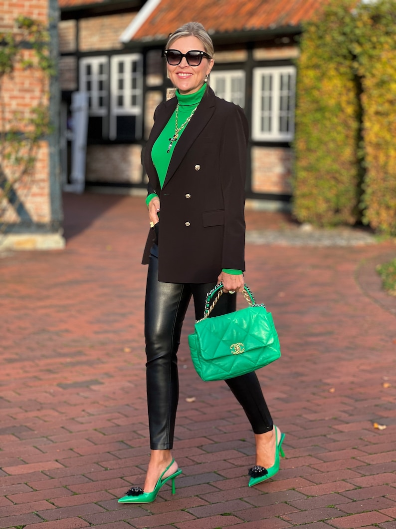 May include: A woman wearing a green turtleneck sweater, a black blazer, black leather trousers, and green heels. She is carrying a green quilted handbag with a gold chain strap.