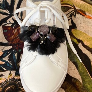 May include: White leather trainers with black feathers and rhinestones on the laces.