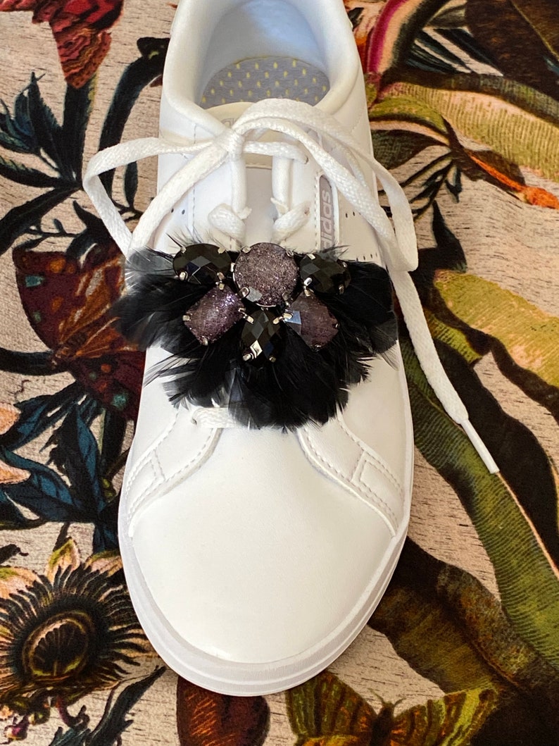 May include: White leather trainers with black feathers and rhinestones on the laces.