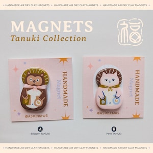 Peut inclure: Deux aimants faits à la main en argile séchée à l'air de la collection Tanuki. L'un est marron, l'autre rose. Chaque aimant présente un design de personnage Tanuki avec le texte "@ASUDRAWS" et "HANDMADE Magnet". Le fond est rose clair avec des étoiles et des diamants.