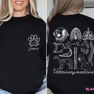 May include: Black sweatshirt with a white paw print, a heartbeat, and the name "Jessica" on the front. The back of the sweatshirt features a white design of various animal anatomy illustrations, including a skull, bones, heart, and intestines. The text "Veterinary medicine" is printed below the design.