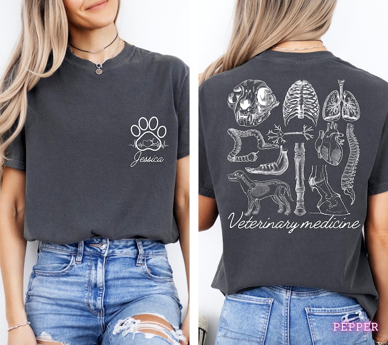 May include: A dark grey t-shirt with a white paw print and heartbeat graphic on the front. The back of the shirt has a white graphic of various animal anatomy illustrations, including a skull, heart, lungs, spine, and bones. The text "Veterinary medicine" is printed below the graphic.
