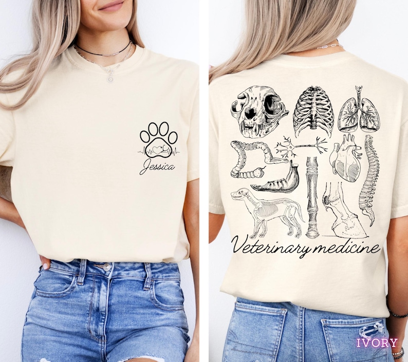 May include: A cream-colored t-shirt with a paw print and heartbeat graphic on the left side and the text "Jessica". The back of the shirt has a black and white illustration of various animal anatomy parts, including a skull, heart, lungs, spine, and bones. The text "Veterinary medicine" is printed below the illustration.