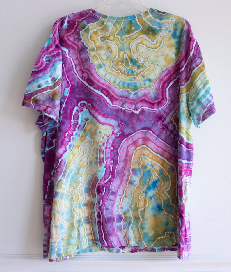 Puede incluir: Una camiseta tie-dye con un patr&oacute;n de remolino de colores rosa, amarillo, azul y verde. La camiseta tiene cuello redondo y mangas cortas.