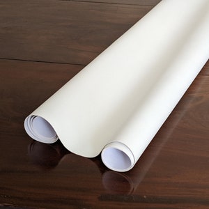 May include: A white roll of paper is rolled up and lying on a wooden surface. The paper is smooth and appears to be a backdrop or background.