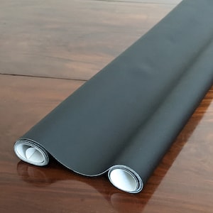 May include: A roll of black fabric with a smooth, matt finish. The fabric is rolled up and the edges are visible.