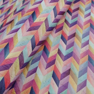 May include: A colourful fabric with a chevron pattern in shades of pink, purple, blue, yellow, and orange. The fabric has a textured surface that resembles cork.
