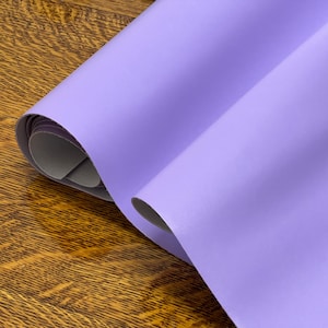 May include: A roll of lavender purple faux leather fabric. The fabric has a smooth, slightly textured surface.