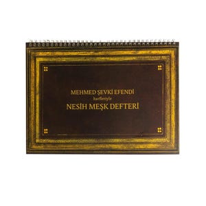 May include: A spiral-bound notebook with a dark brown cover and gold-colored decorative border. The cover features text in gold lettering, including the name "MEHMED ŞEVKİ EFENDİ" and "NESİH MEŞK DEFTERİ".