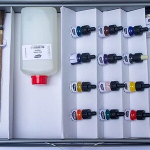 Pode incluir: Um conjunto de 12 frascos de tinta em várias cores, incluindo azul, verde, vermelho, amarelo e preto. Os frascos são organizados em filas de quatro, e cada frasco tem um conta-gotas. Também há um frasco de diluente de tinta e um pincel na imagem.